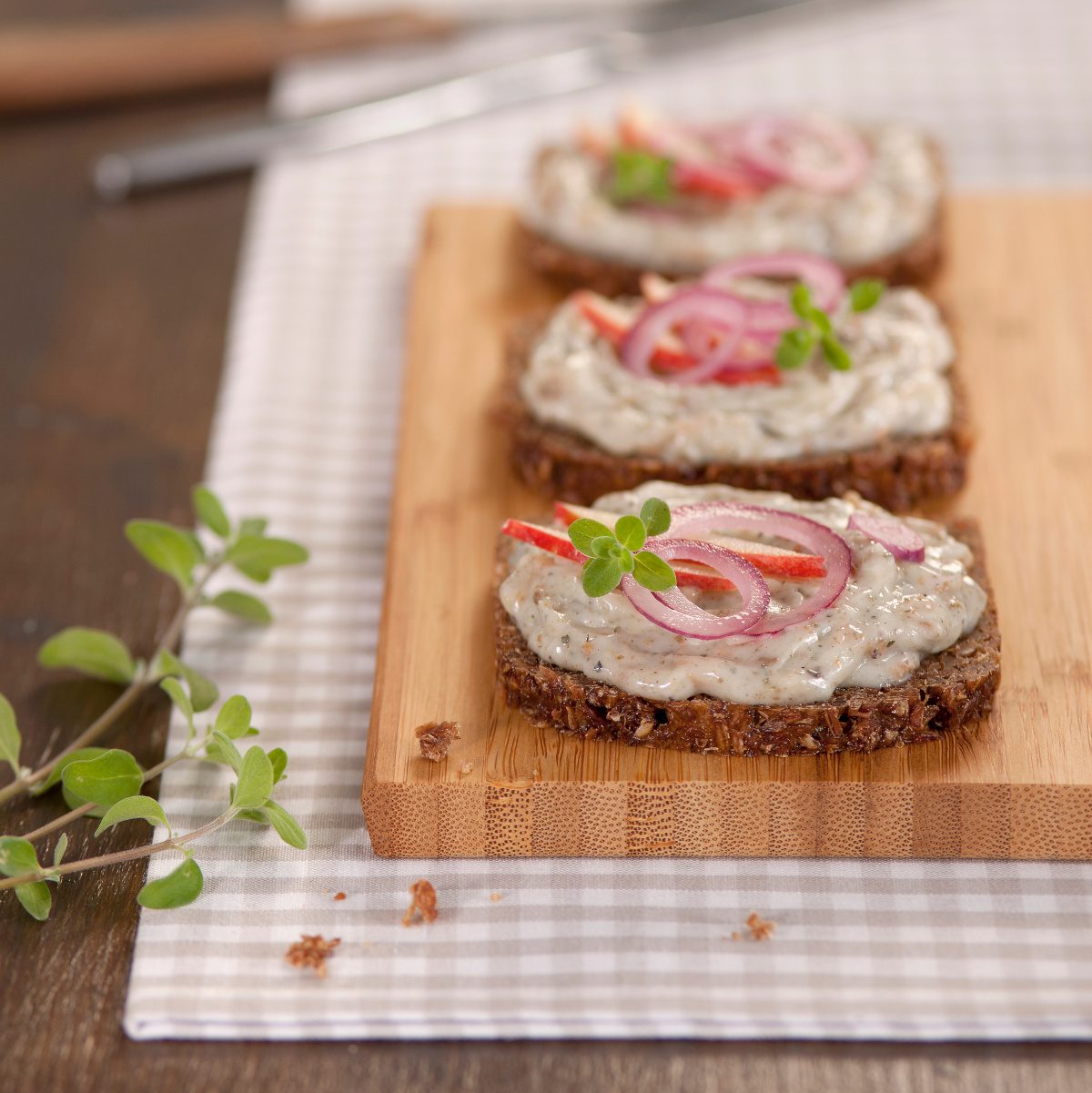 Gänsegriebenschmalz der Goosies Wurstwarenmanufaktur, dekoriert mit drei bestrichenen Scheiben Brot mit Zwiebeln auf einem Brettchen