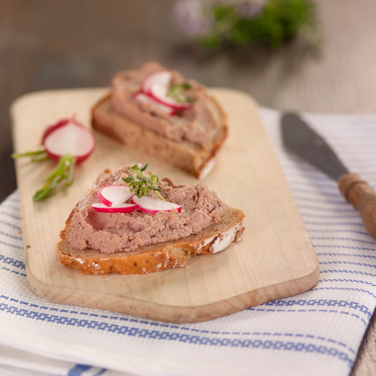 Gänseleberwurst der Goosies Wurstwarenmanufaktur, dekoriert mit zwei bestrichenen Scheiben Brot mit Radieschen auf einem Brettchen
