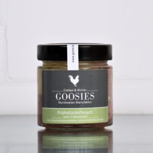 Hähnchen-Frühstücksfleisch der Goosies Wurstwarenmanufaktur im 175-g-Glas, auf einem Edelstahltisch vor weißem Hintergrund