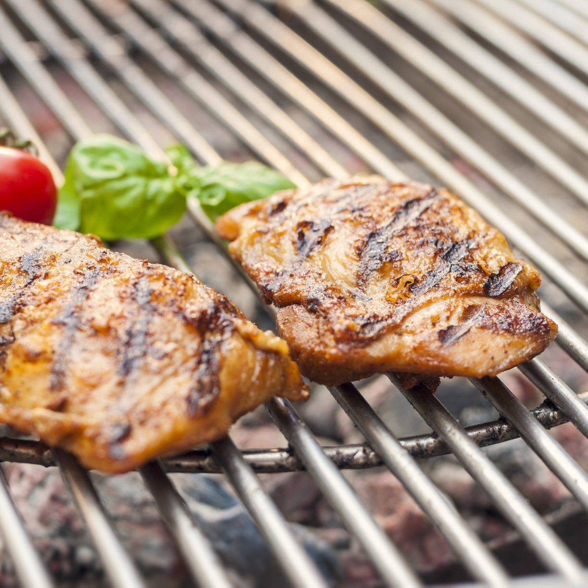 Sous-vide gegartes Grill-Hähnchensteak der Goosies Wurstwarenmanufaktur, dekoriert auf einem Grill mit Tomaten und Basilikum