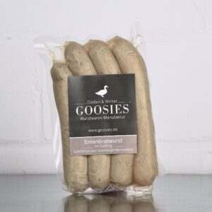 Entenbratwurst der Goosies Wurstwarenmanufaktur in einer 225-g-Packung mit vier Würstchen, auf einem Edelstahltisch vor weißem Hintergrund