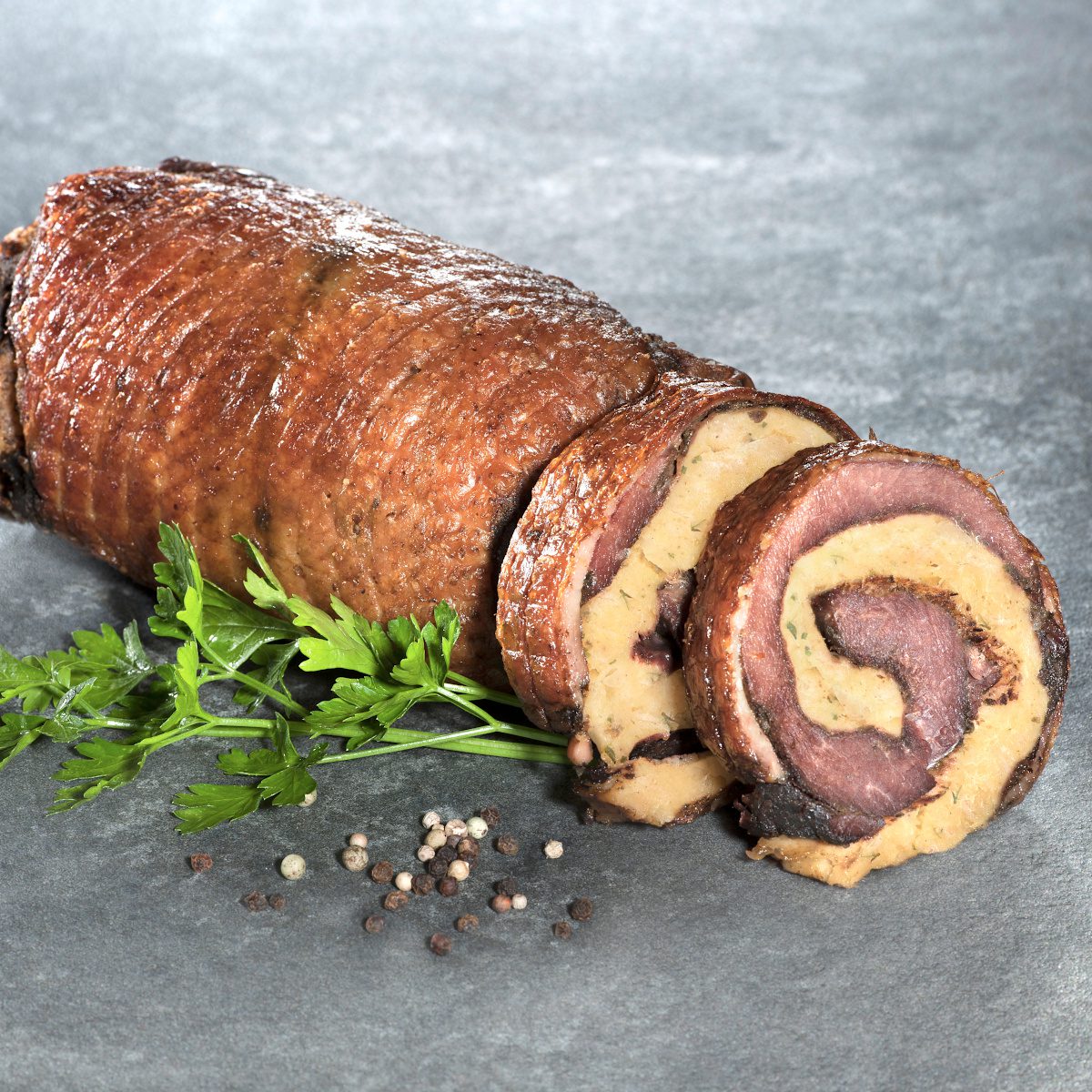 Sous-vide gegarter Gänserollbraten mit Semmelknödelfüllung der Goosies Wurstwarenmanufaktur, dekoriert auf einer Steinplatte mit Petersilie und Pfefferkörnern
