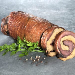 Sous-vide gegarter Gänserollbraten mit Semmelknödelfüllung der Goosies Wurstwarenmanufaktur, dekoriert auf einer Steinplatte mit Petersilie und Pfefferkörnern