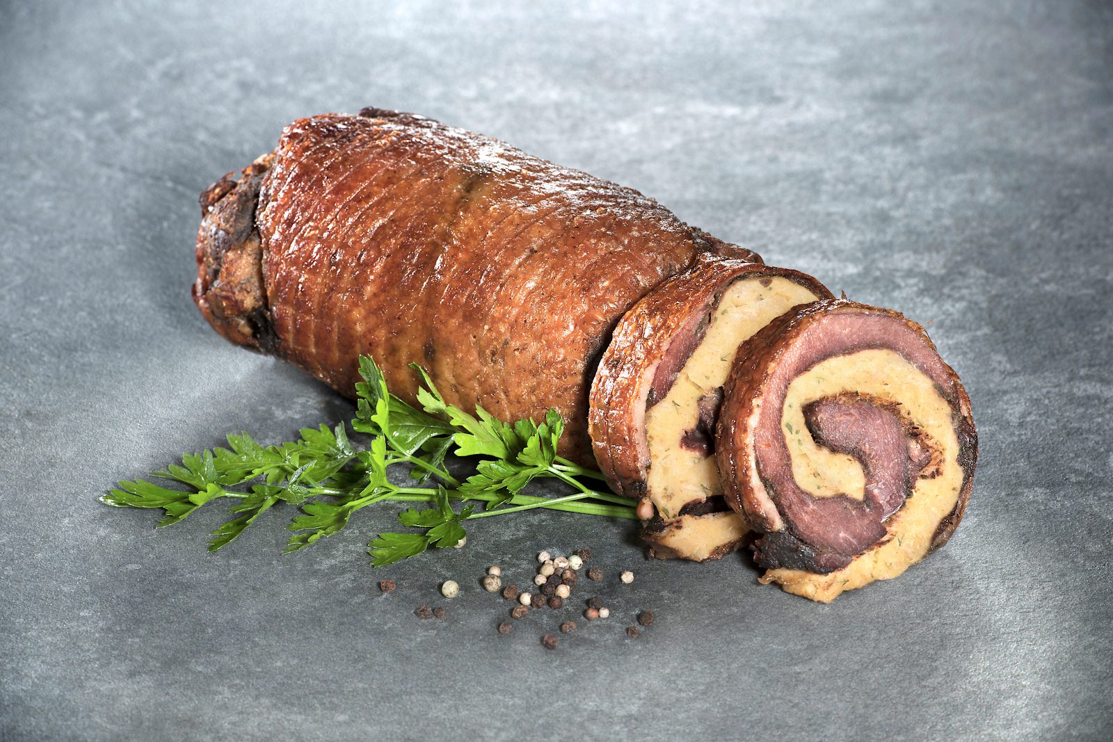 Sous-vide gegarter Gänserollbraten mit Semmelknödelfüllung der Goosies Wurstwarenmanufaktur, dekoriert auf einer Steinplatte mit Petersilie und Pfefferkörnern