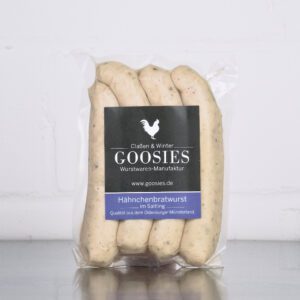 Hähnchenbratwurst der Goosies Wurstwarenmanufaktur in einer 225-g-Packung mit vier Würstchen, auf einem Edelstahltisch vor weißem Hintergrund