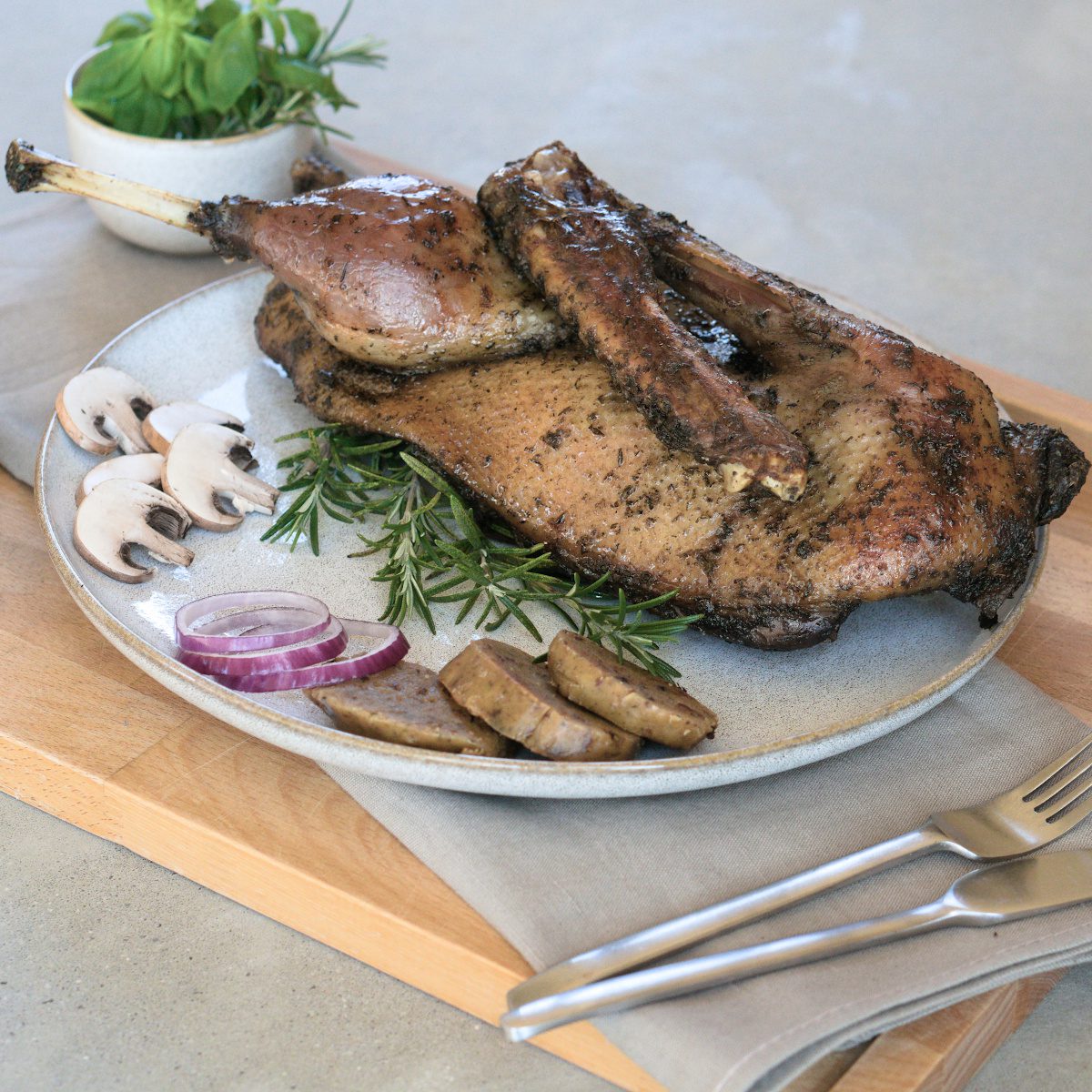 Sous-vide gegarte halbe Gans der Goosies Wurstwarenmanufaktur, dekoriert auf einem Brett mit Knödelscheiben, Salat, Pilzen, Zwiebeln und Rosmarin