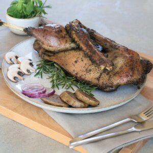 Sous-vide gegarte halbe Gans der Goosies Wurstwarenmanufaktur, dekoriert auf einem Brett mit Knödelscheiben, Salat, Pilzen, Zwiebeln und Rosmarin