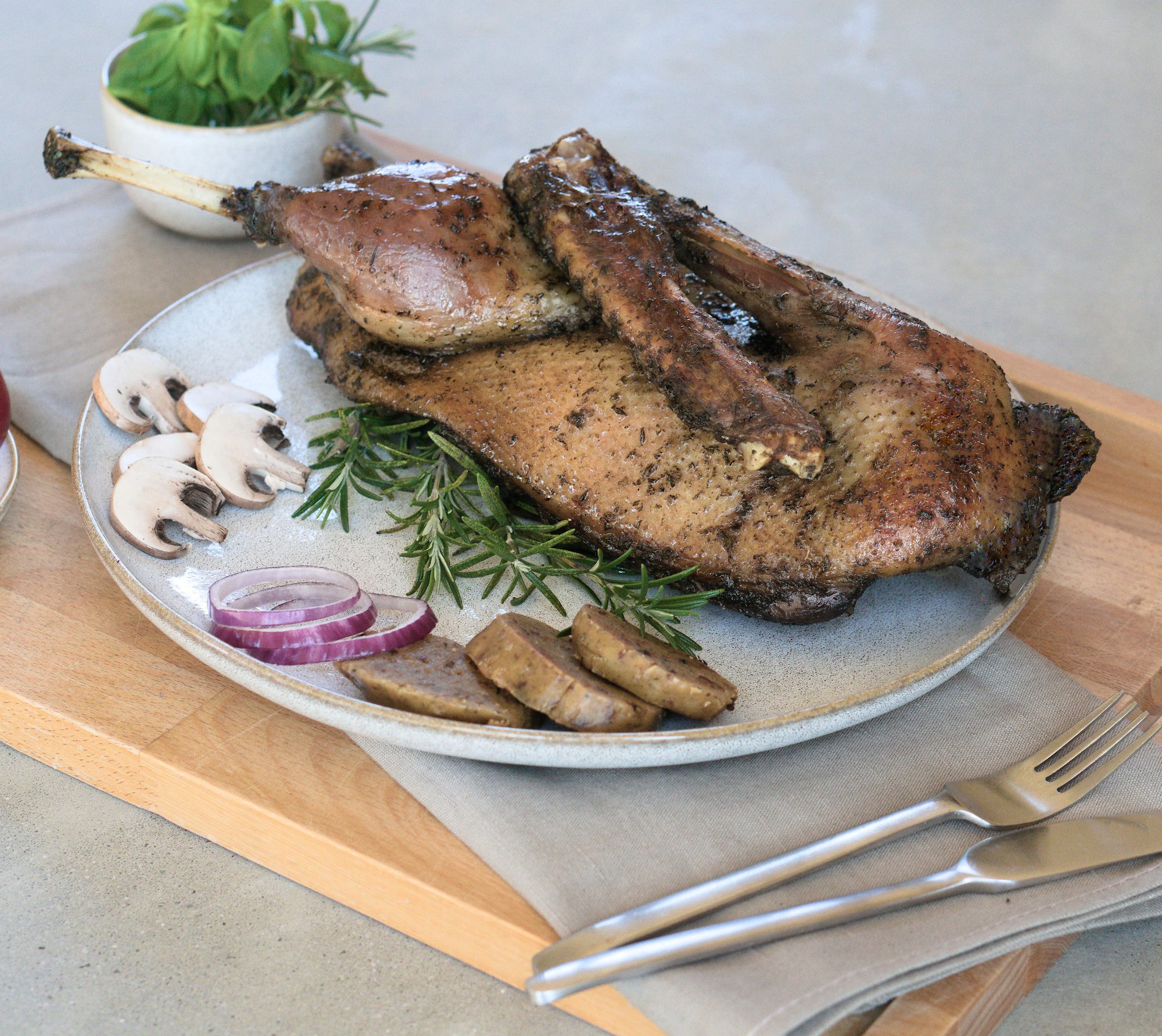 Sous-vide gegarte halbe Gans der Goosies Wurstwarenmanufaktur, dekoriert auf einem Brett mit Knödelscheiben, Salat, Pilzen, Zwiebeln und Rosmarin